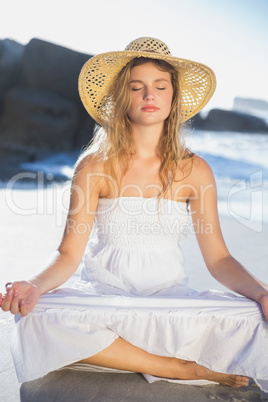 Beautiful blonde in sundress sitting in lotus pose on the beach