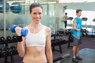 Fit smiling brunette lifting heavy black dumbbell