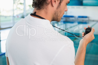 Swimming coach standing by the pool looking at stopwatch