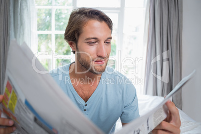 Handsome man sitting on bed reading the newspaper