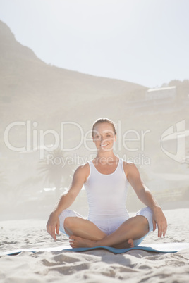 Smiling woman sitting in lotus pose on beach