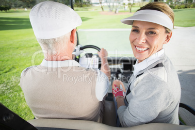 Golfing couple driving in their golf buggy with woman smiling at