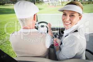 Golfing couple driving in their golf buggy with woman smiling at