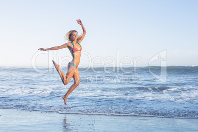 Happy blonde leaping on the beach in bikini