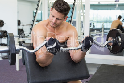 Shirtless focused bodybuilder lifting heavy barbell weight using