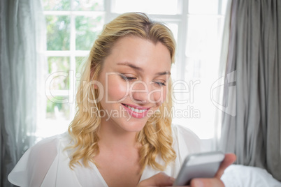 Pretty blonde sitting on bed texting on the phone