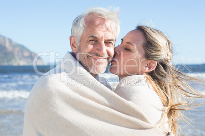 Smiling couple wrapped up in blanket on the beach