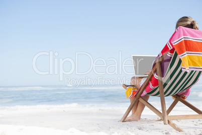 Woman sitting on beach in deck chair using laptop