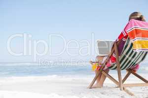 Woman sitting on beach in deck chair using laptop