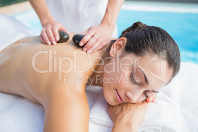 Happy brunette getting a hot stone massage poolside