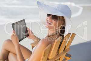Woman in straw hat relaxing in deck chair on the beach using tab