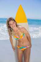 Beautiful smiling surfer girl standing on the beach with her sur