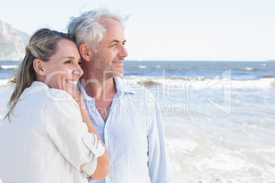 Happy couple hugging on the beach looking out to sea