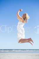 Blonde in white dress smiling at camera and leaping on the beach