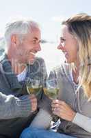 Couple enjoying white wine on picnic at the beach smiling at eac