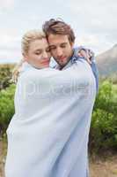 Cute affectionate couple standing outside wrapped in blanket