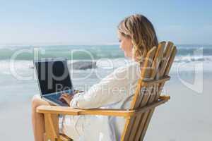 Gorgeous blonde sitting on deck chair using laptop on beach