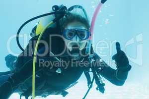 Woman on scuba training submerged in swimming pool showing thumb