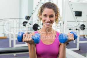 Pretty fit woman lifting blue dumbbells smiling at camera