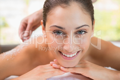 Beauty therapist pouring salt scrub on smiling womans back