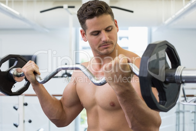 Shirtless focused bodybuilder lifting heavy barbell weight