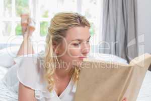 Pretty blonde lying on bed reading a book