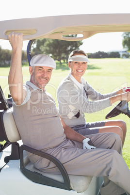 Happy golfing couple smiling at camera in their buggy