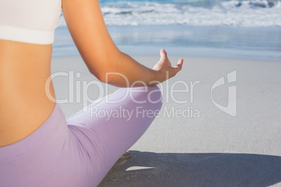 Sporty blonde sitting in lotus pose on the beach