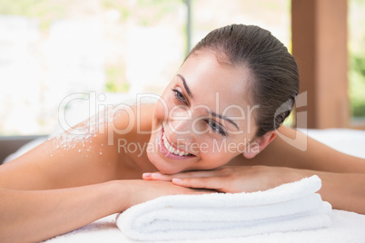 Beautiful smiling brunette lying on massage table with salt scru