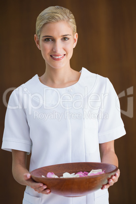 Smiling beauty therapist holding bowl of rose petals