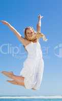 Pretty carefree blonde jumping and smiling at camera on the beac