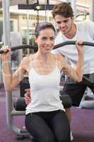 Fit brunette using weights machine for arms with trainer helping