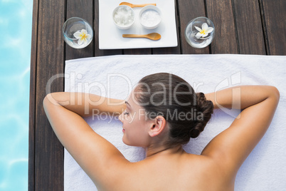 Tranquil brunette lying on towel poolside with beauty treatments