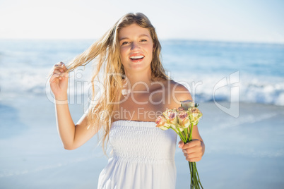 Beautiful blonde in sundress holding roses on the beach