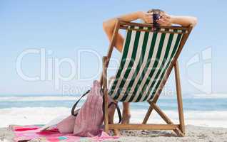 Woman sitting in deck chair at the beach with her beach bag and