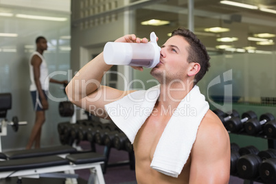 Shirtless bodybuilder drinking protein drink sitting on bench