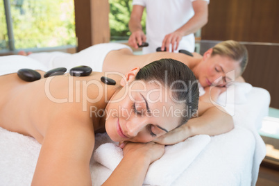 Calm friends lying on massage tables with hot stones on their ba