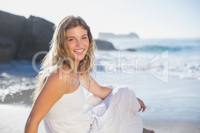 Beautiful smiling blonde in sundress sitting on the beach