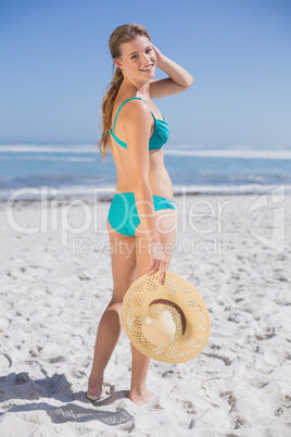 Pretty smiling woman in bikini on beach holding sunhat