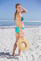 Pretty smiling woman in bikini on beach holding sunhat
