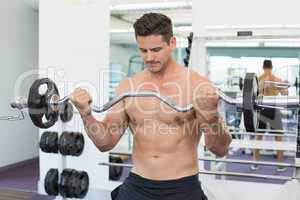 Shirtless focused bodybuilder lifting heavy barbell weight
