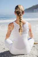Blonde woman sitting in lotus pose on beach