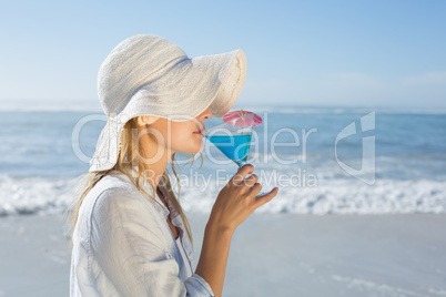 Smiling blonde relaxing by the sea sipping cocktail