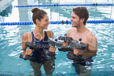 Man and woman standing with foam dumbbells in the pool