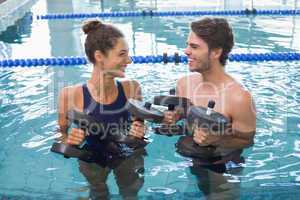 Man and woman standing with foam dumbbells in the pool