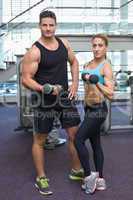 Bodybuilding man and woman holding dumbbells looking at camera