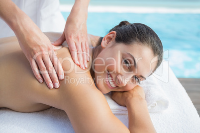 Smiling brunette getting a massage poolside looking at camera