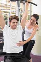 Fit man using weights machine for arms with his trainer