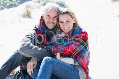 Happy couple wrapped up in blanket sitting on the beach