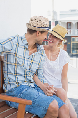 Young hip couple sitting on bench smiling at each other